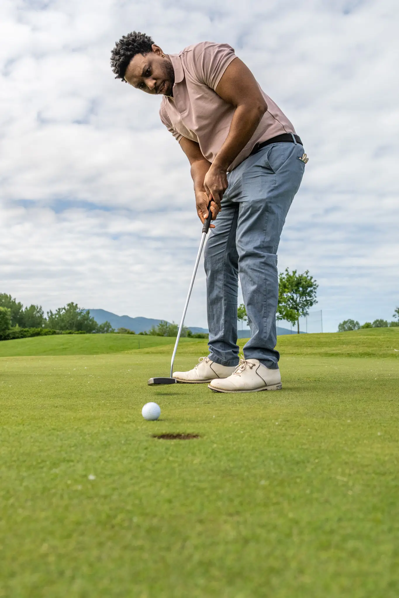 Golfer preparing to putt on a green golf course under a cloudy sky.